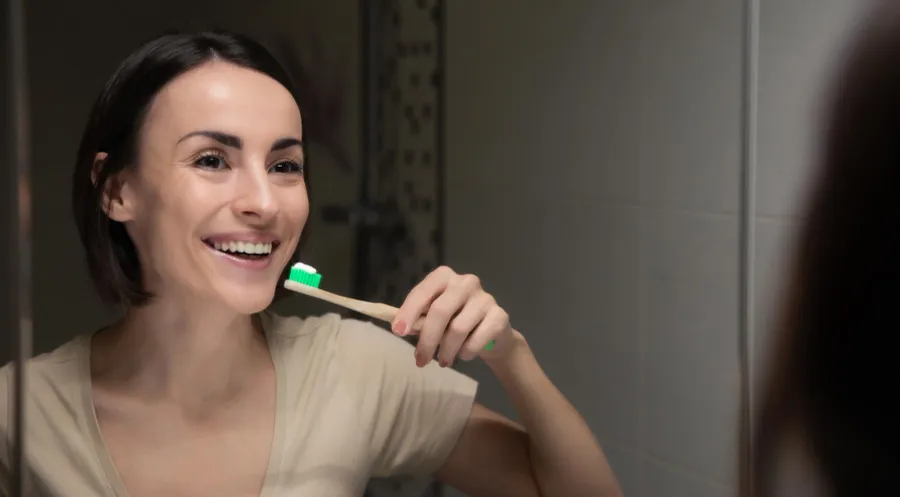 Mujer sonriendo frente al espejo mientras se cepilla los dientes
