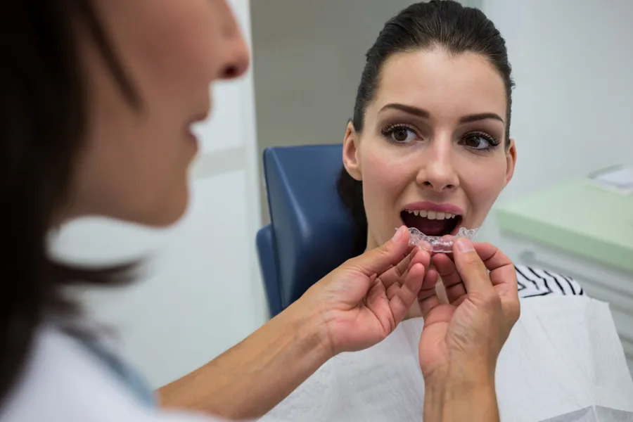 Dentista colocando una férula de descarga transparente a medida en los dientes de una paciente